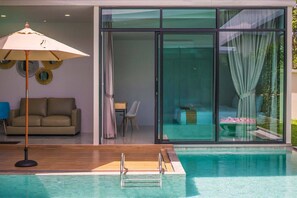 A modern indoor swimming pool with a wooden deck, a sofa, and a dining area with a table and chairs. - Goodnight Phuket Villa (Wichit)