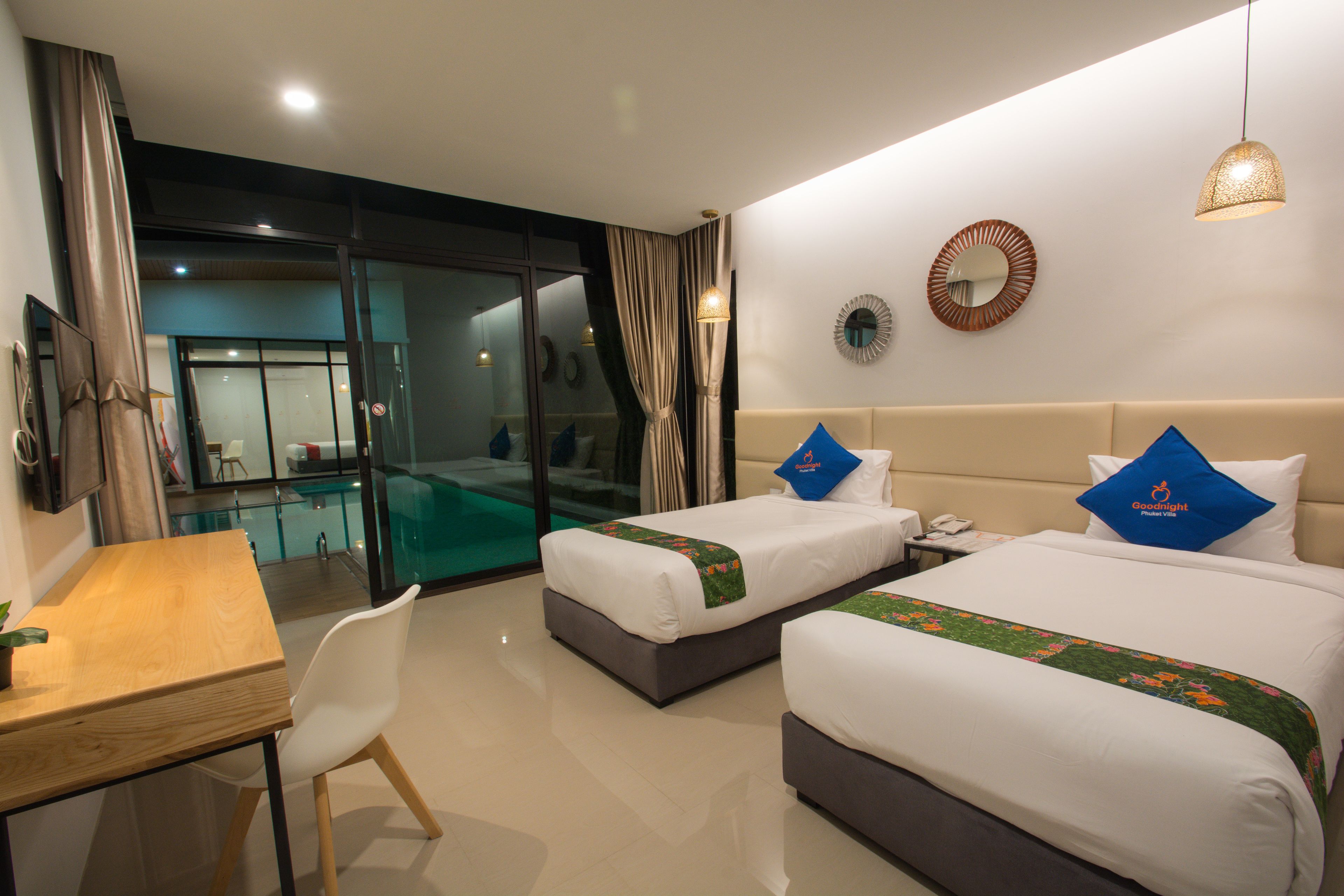 A hotel room with two beds, a desk, a chair, a mirror, and a view of a pool area.