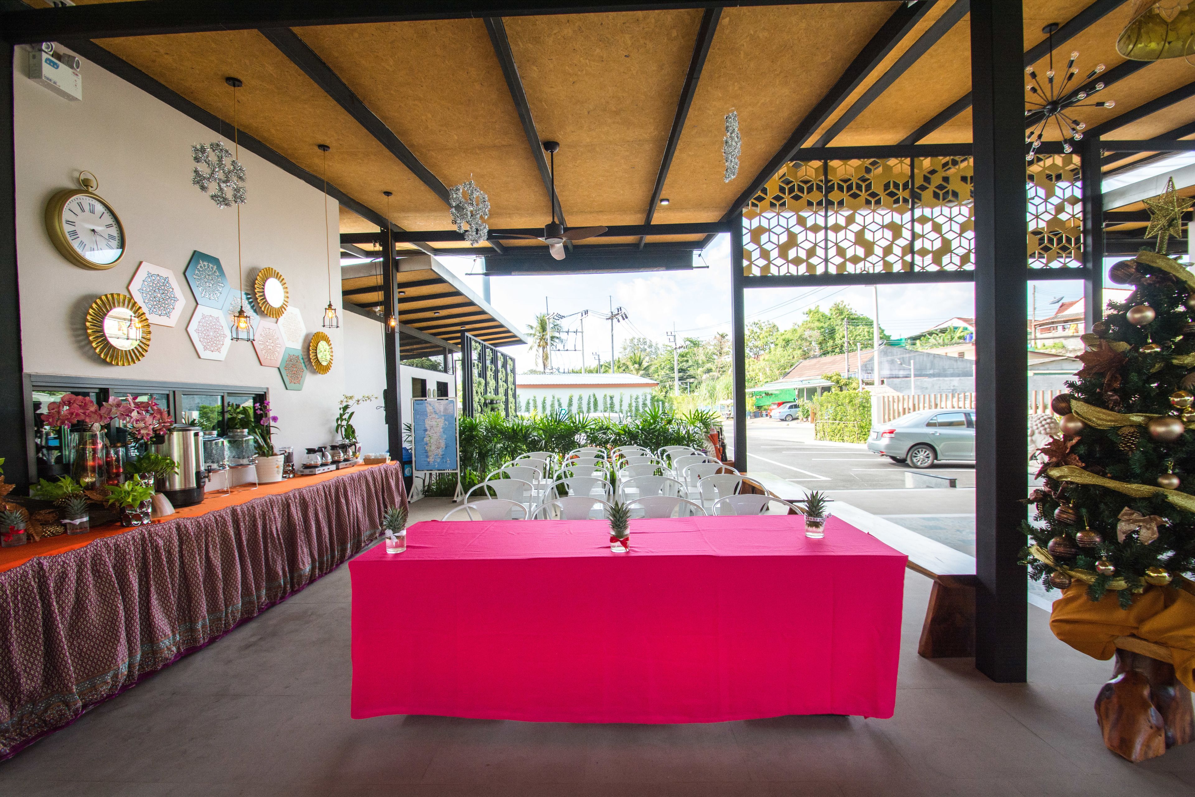 Una habitación con una larga mesa cubierta con un mantel rosa brillante, rodeada de sillas blancas. Las paredes están decoradas con varias obras de arte y relojes enmarcados.