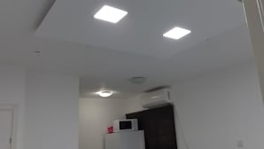 Un pasillo estrecho con paredes blancas, un techo con iluminación empotrada y un microondas sobre un electrodoméstico blanco.