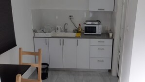 Una cocina compacta con armarios blancos, un microondas, una tetera y un lavabo.