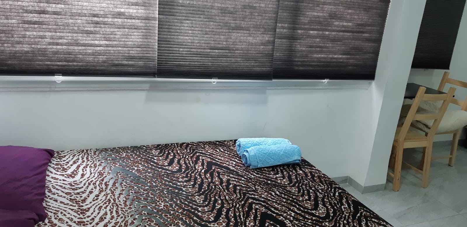 A bedroom with a patterned bedspread, a rolled-up towel, and a wooden chair.