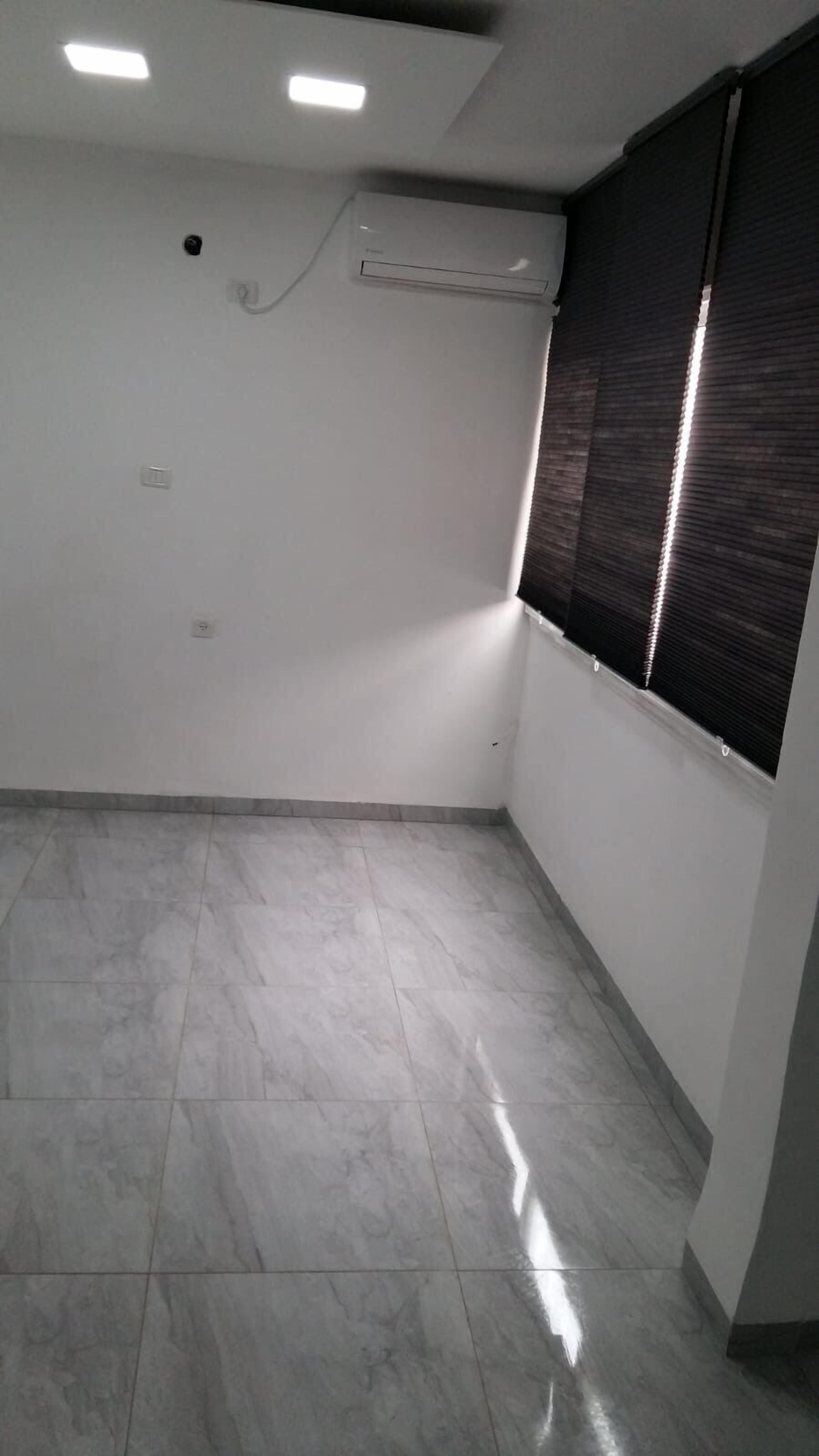 A room with a tiled floor, a window with blinds, an air conditioning unit, and a ceiling light fixture.