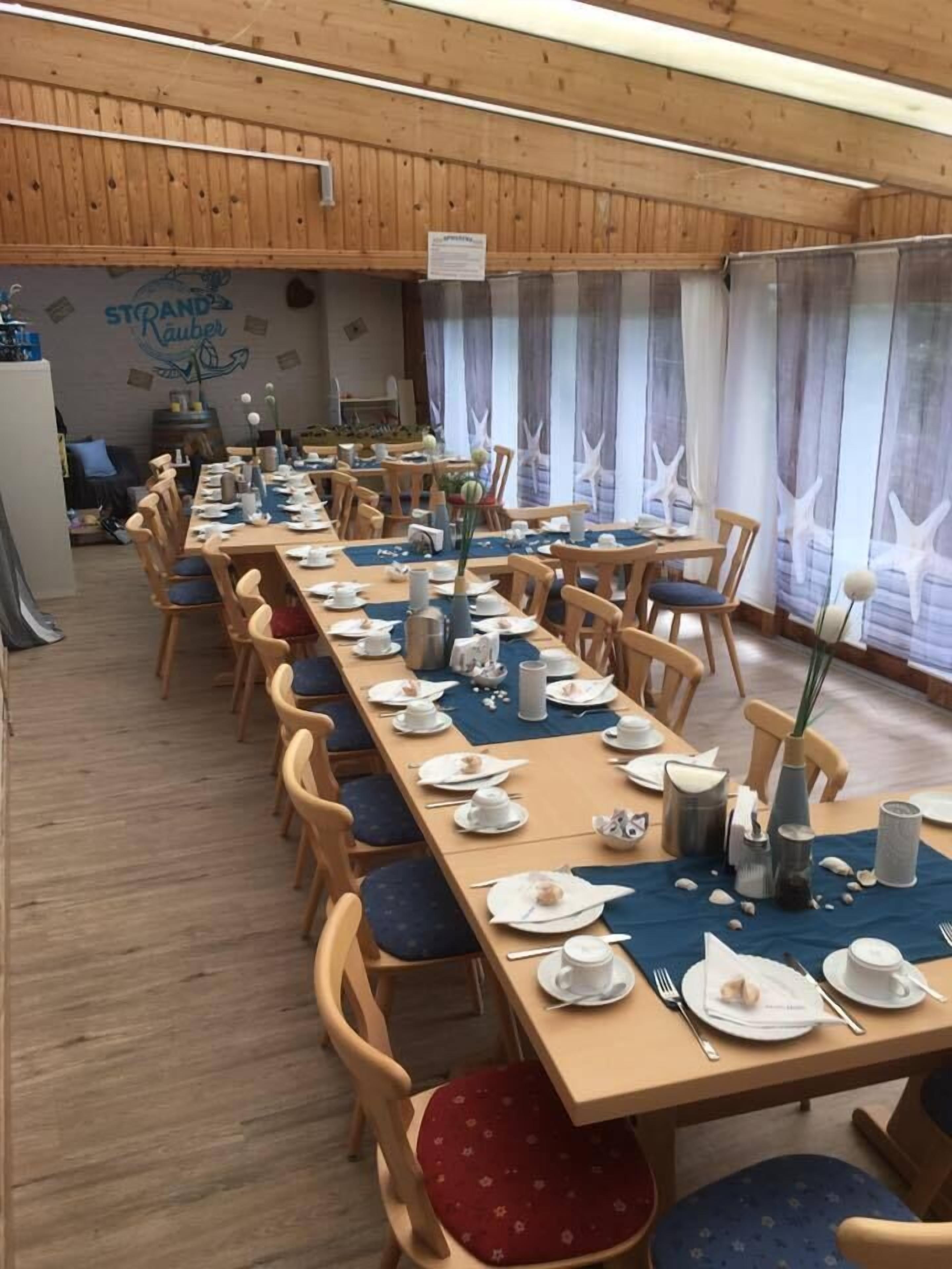 A long dining table set with chairs, a wooden ceiling, and a wall with a nautical theme.