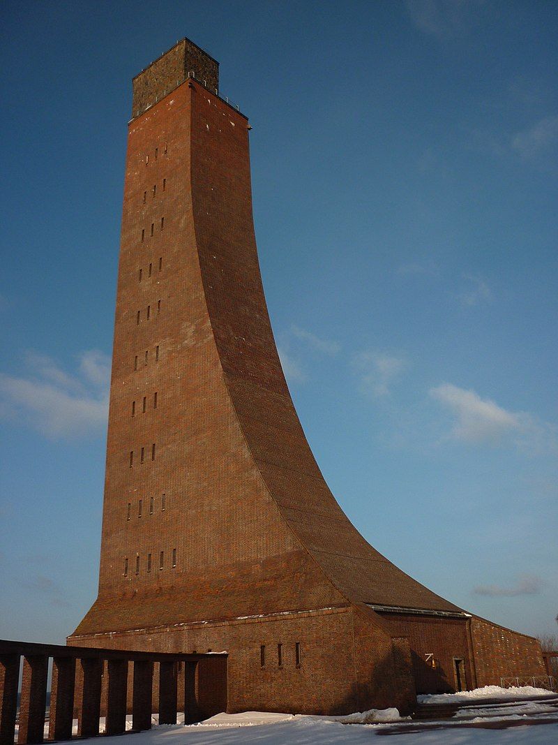 Uma torre de tijolos alta e curva com telhado plano e várias janelas.