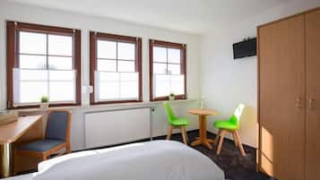 A hotel room with a bed, a desk, two chairs, a small table, and a wardrobe.