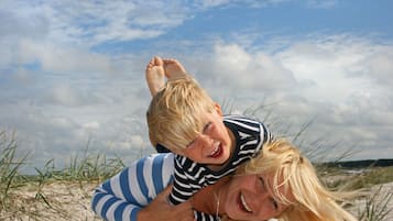 A person carrying another on their back, with a sandy beach and dunes in the background.