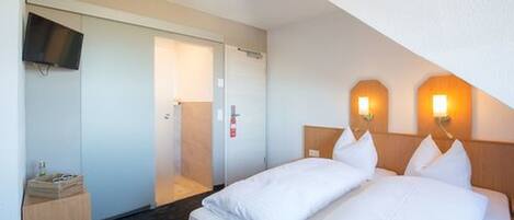A hotel room with a bed, a TV mounted on the wall, and a wooden nightstand.