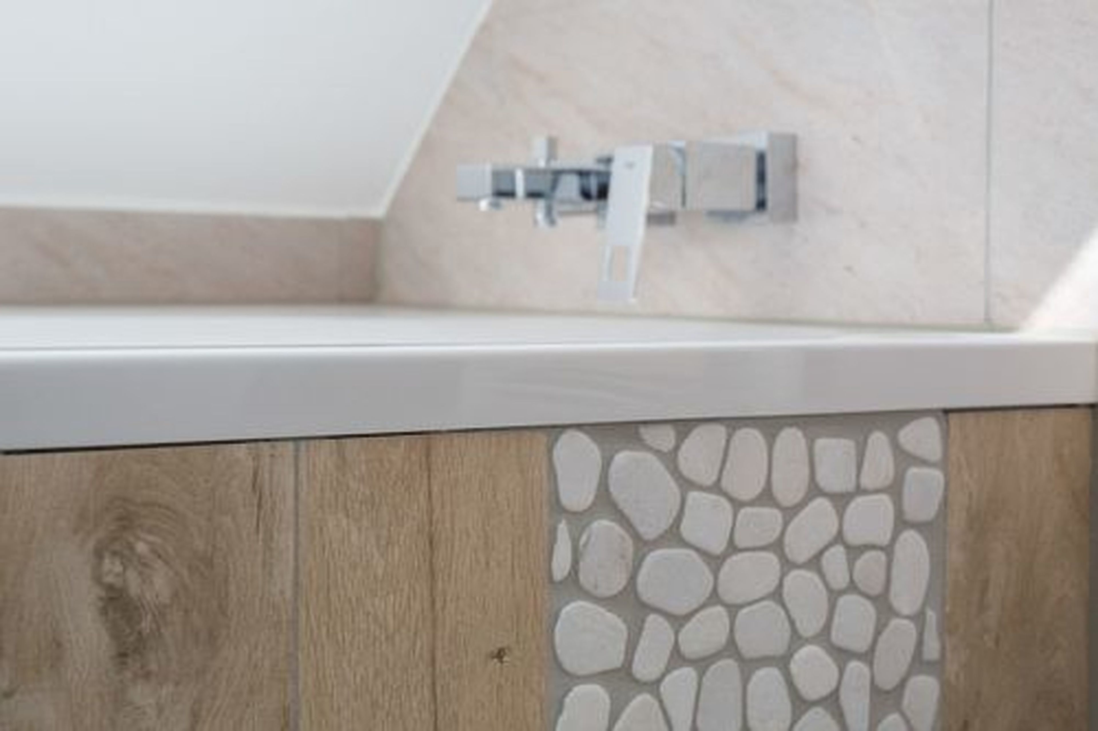 Une salle de bain avec un comptoir blanc, un panneau en bois à motif pierre et un porte-serviettes métallique.