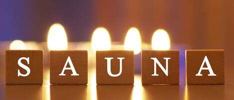 Wooden blocks with letters spelling "SAUNA" in white, with a blurred background of lights.