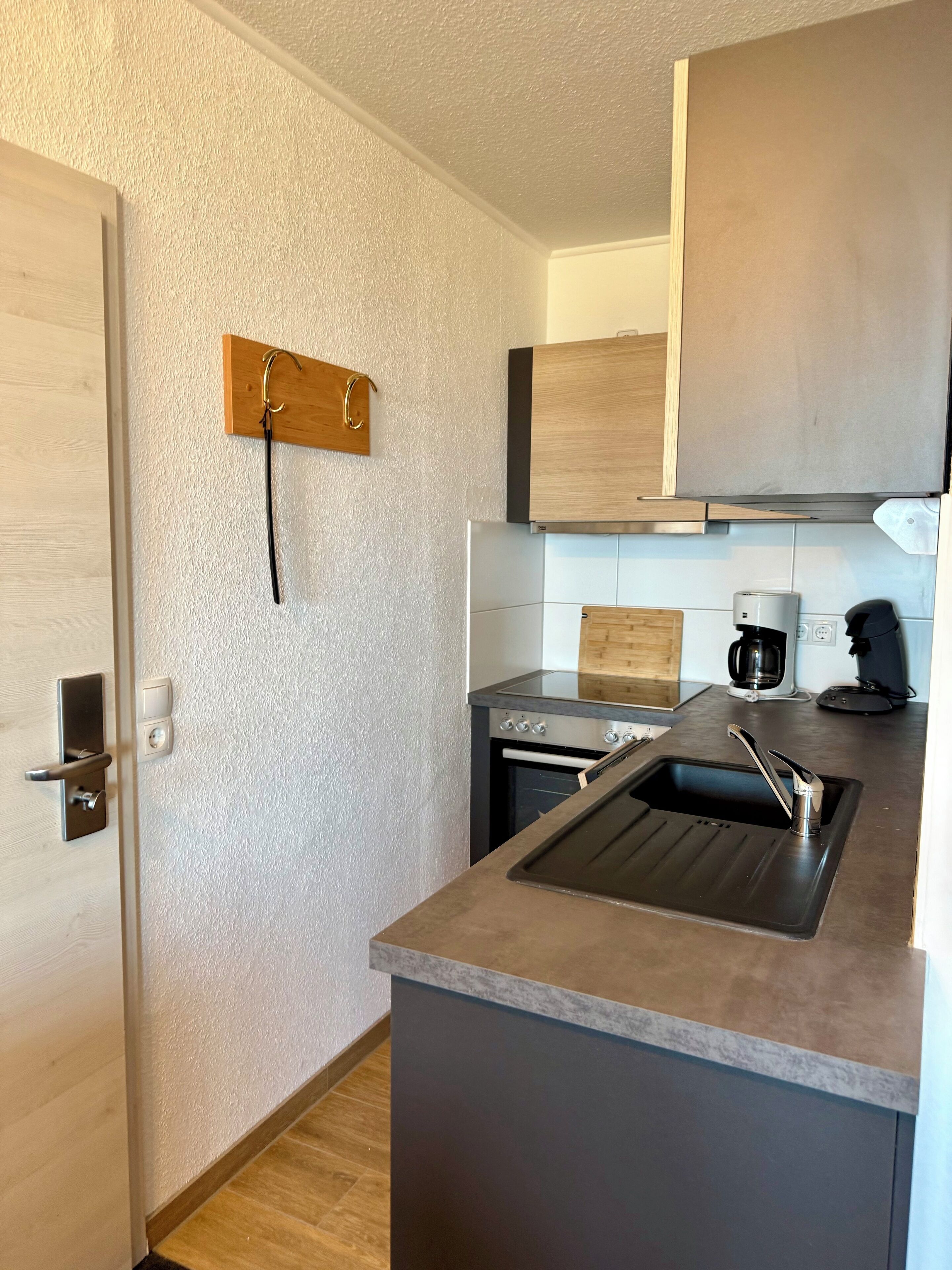 A modern kitchen with a built-in oven, a stainless steel sink, and wooden cabinets.