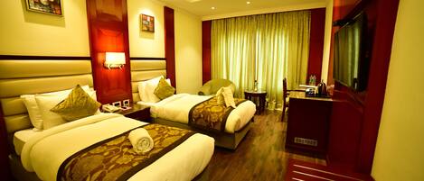 A hotel room with two beds, a desk, a TV, and a bathroom.