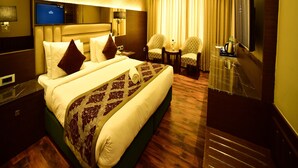 A hotel room with a large bed, two armchairs, a small table, a TV, and a minibar. - Hotel Milan Palace (Prayagraj)
