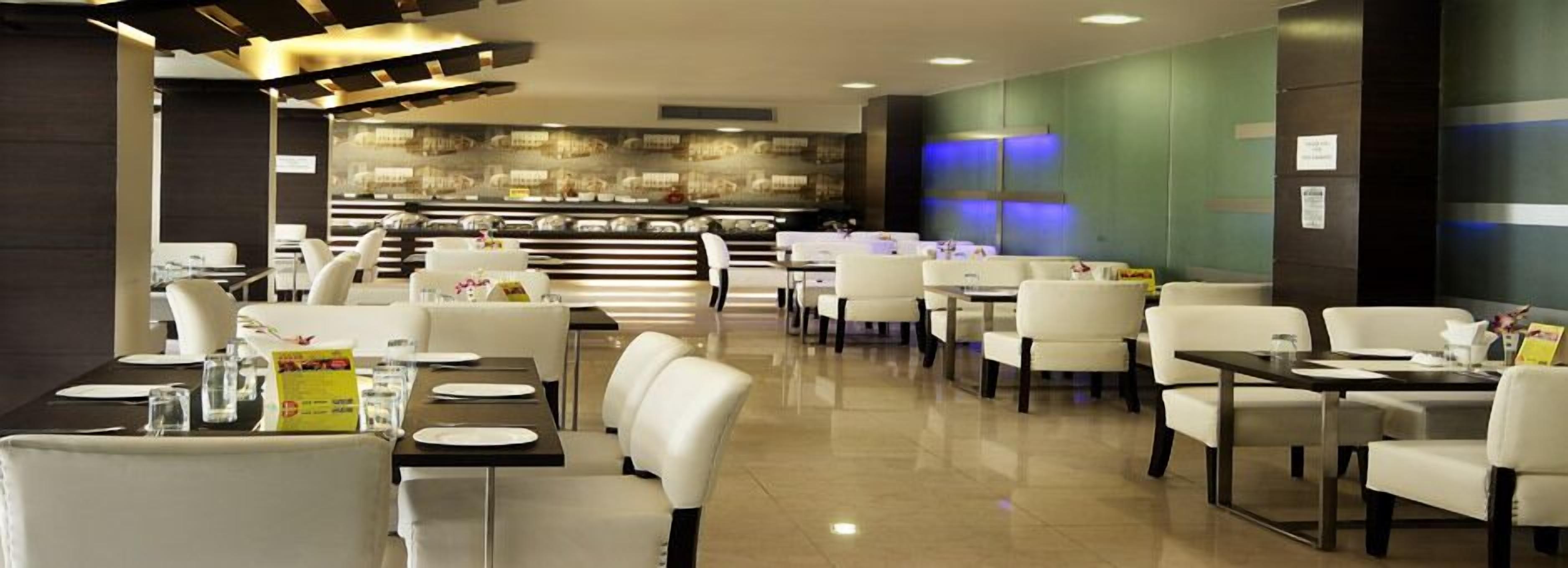 A modern restaurant with white chairs and tables, a central counter with a display case, and a green accent wall.