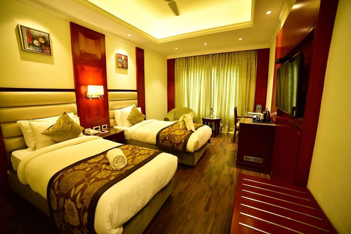 A hotel room with two beds, a desk, a chair, a TV, and a window with curtains.