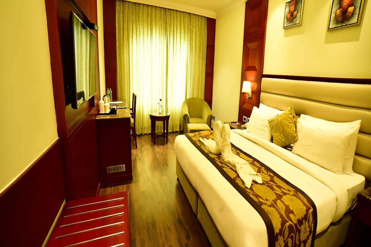 A hotel room with a large bed, a desk, a chair, a small table, and a mirror.