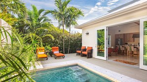 Un espace aménagé au bord de la piscine, comprenant une piscine, des sièges d’extérieur et une vue sur une cuisine moderne.