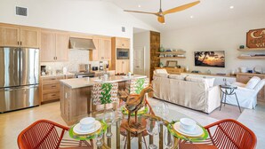 Une cuisine moderne équipée d’appareils électroménagers en acier inoxydable, un coin repas avec une table en verre et un espace salon confortable avec un canapé et des fauteuils.