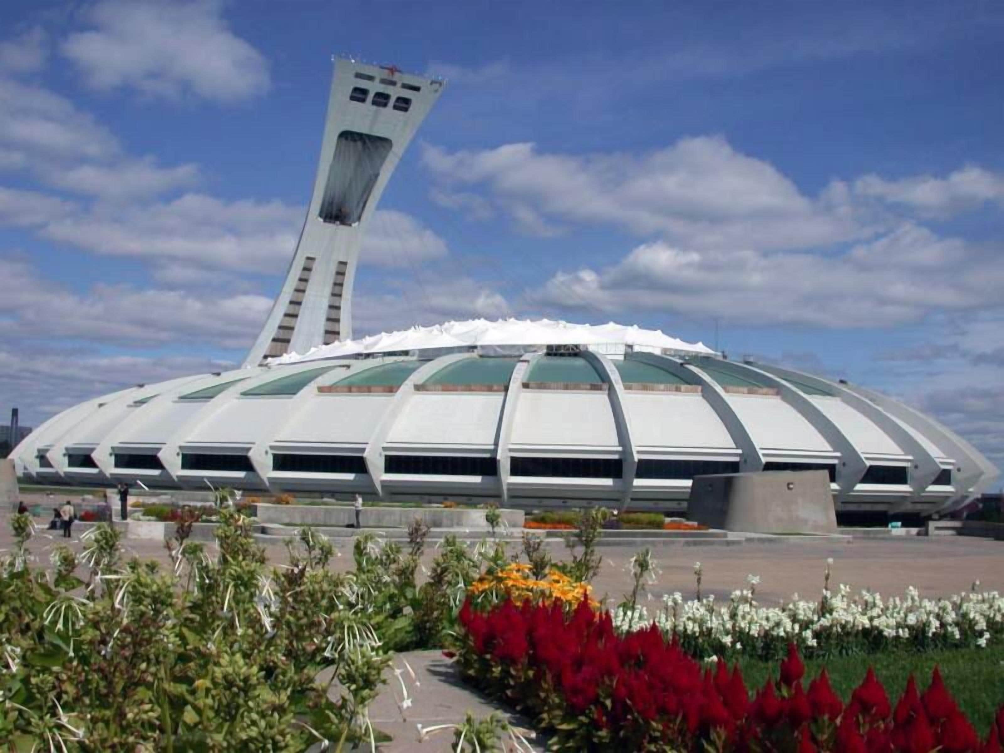 A modern stadium with a unique architectural design, featuring a large central tower and multiple sections with green roofs.