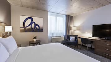 A hotel room with a large bed, a desk with a chair, a television, and a wall-mounted air conditioner.