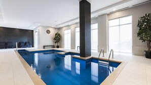 Una amplia piscina cubierta con agua cristalina, rodeada de paredes de azulejos y grandes ventanales que permiten la entrada de luz natural.