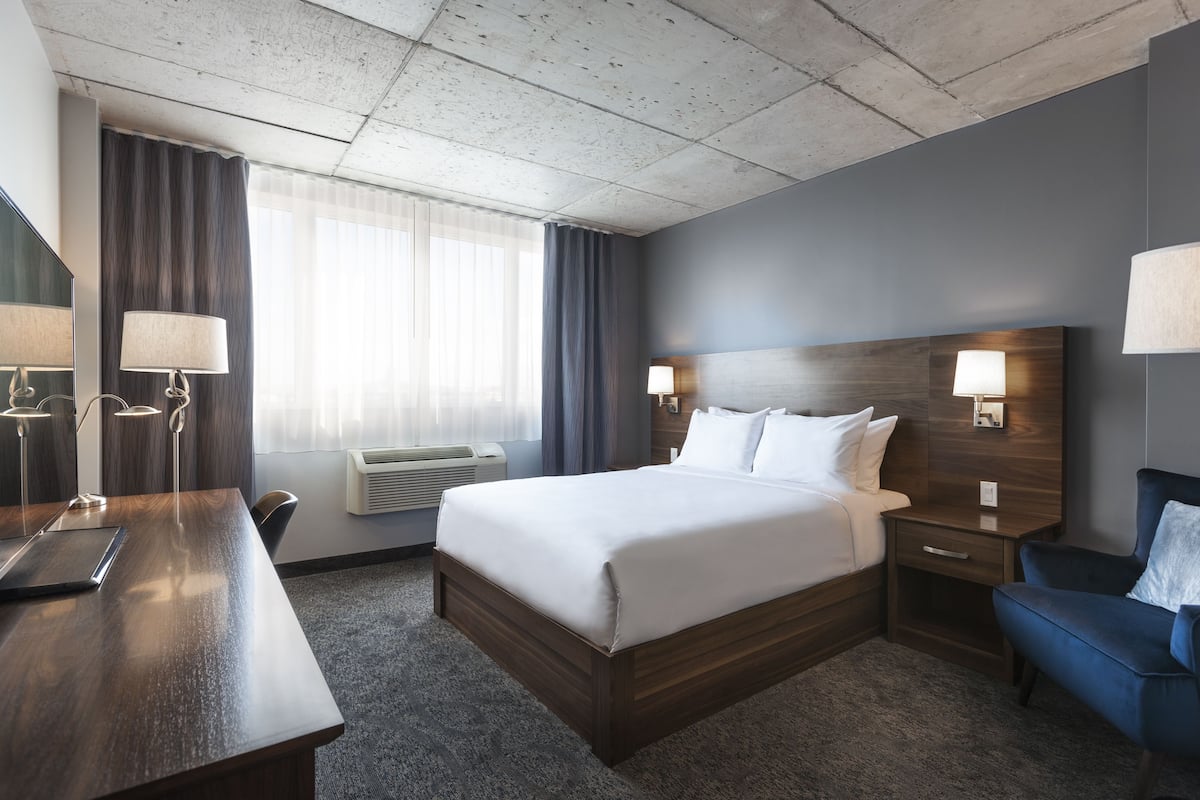 Habitación de hotel con una cama grande, un escritorio, una silla, una mesita de noche y una lámpara.