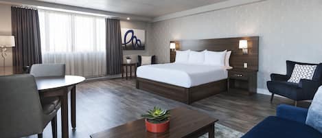 A hotel room with a large bed, a desk, a chair, a sofa, and a potted plant.