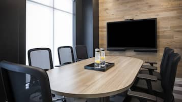 A conference room with a large table, six chairs, a TV on the wall, and a window providing natural light.