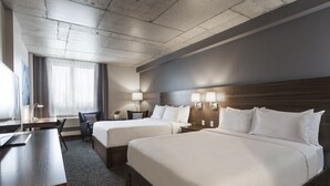 Habitación de hotel con dos camas, un escritorio, una silla y una ventana con cortinas.