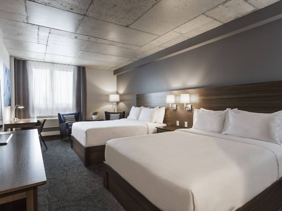 Habitación de hotel con dos camas, un escritorio, una silla y una ventana con cortinas.