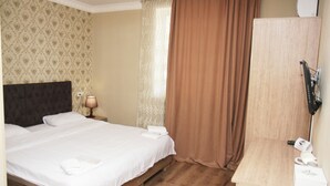 Una habitación de hotel con cama, mesita de noche con lámpara, un escritorio de madera y un espejo.
