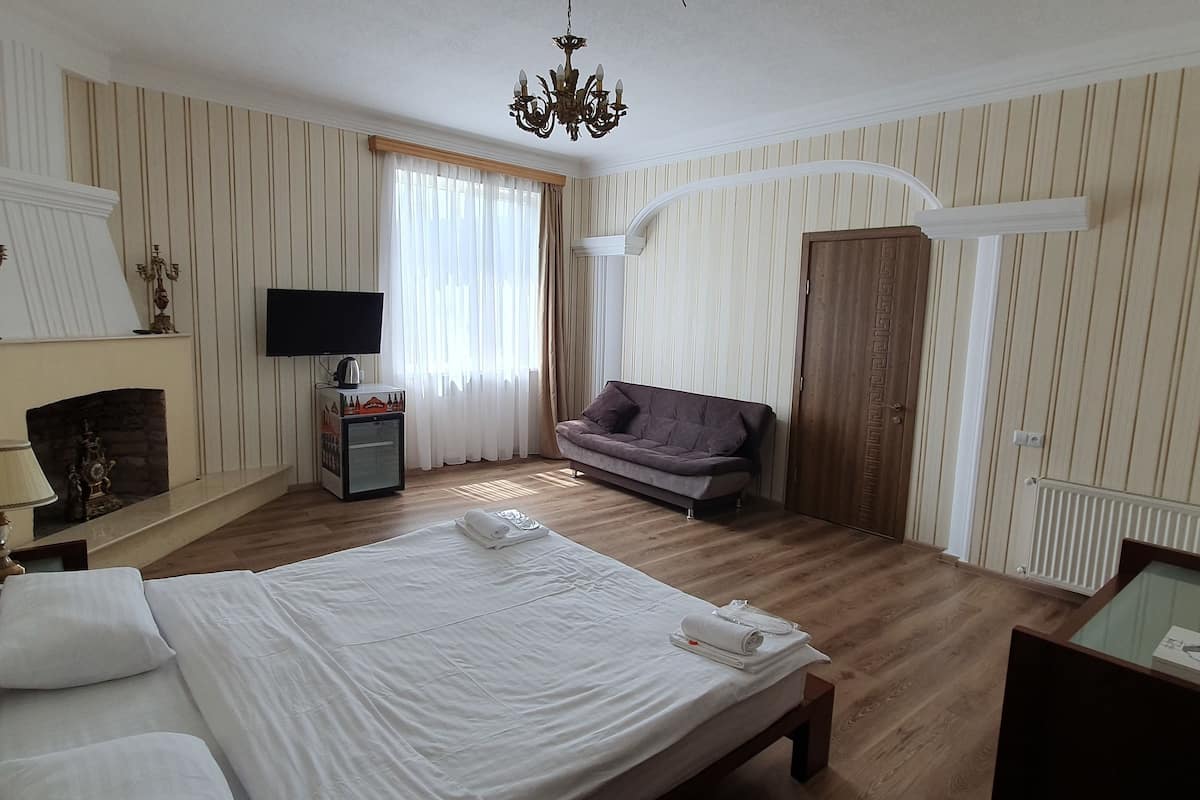 A hotel room with a large bed, a sofa, a TV, a fireplace, and a wooden floor.