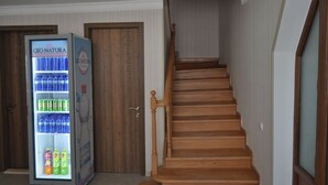 Una escalera de madera con barandilla, una máquina expendedora con agua embotellada y refrescos, y una puerta de madera.