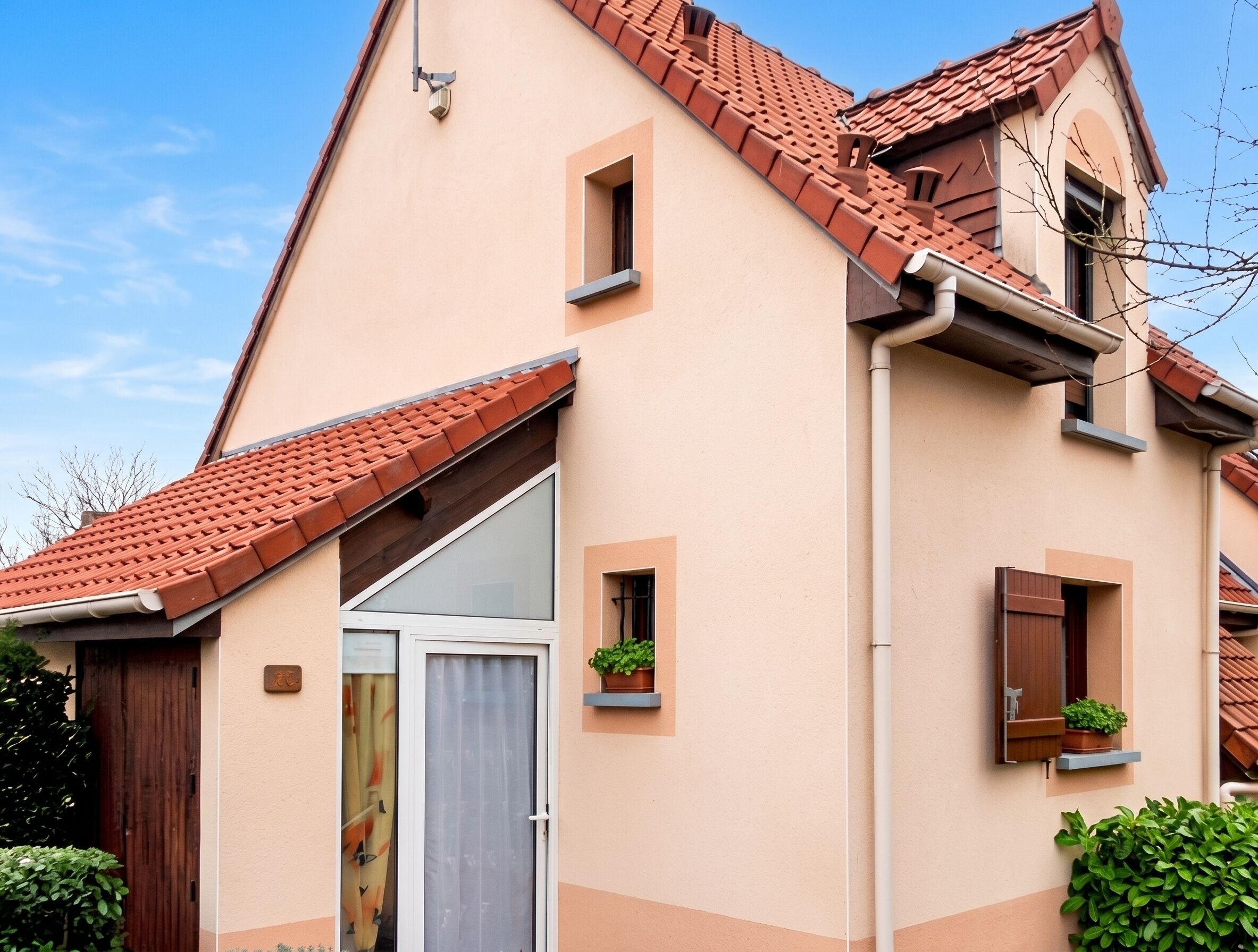 A two-story building with a tiled roof, a sliding glass door, and small windows with shutters.