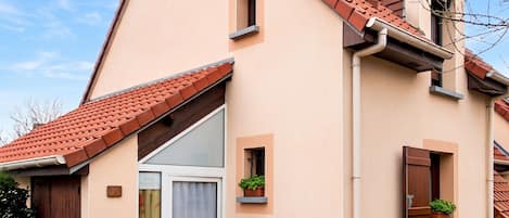 A two-story building with a tiled roof, a sliding glass door, and small windows with shutters.