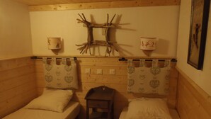 Una habitación pequeña y acogedora con dos camas individuales, cabecero de madera, cortinas con estampado de corazones y una mesita.