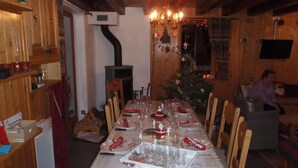 Un comedor con una larga mesa dispuesta para una comida, sillas de madera, un árbol de Navidad y una chimenea.