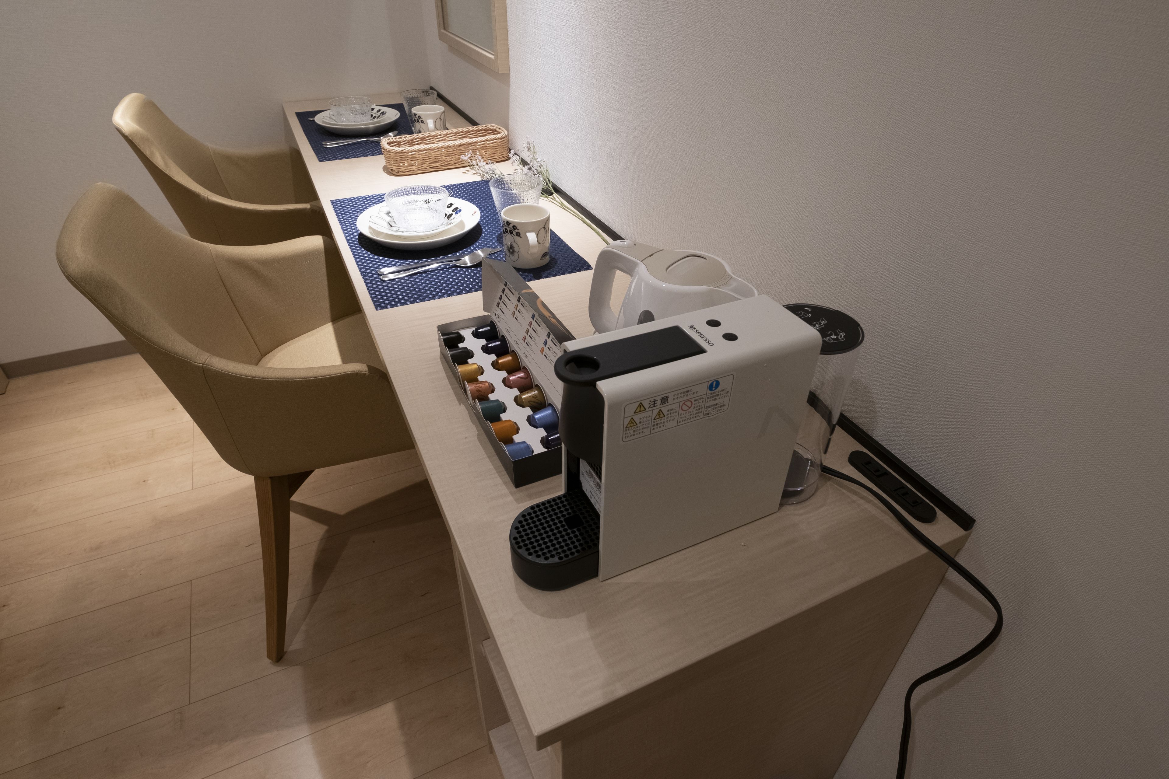 A dining area with a table set for two, a coffee machine, and a basket of bread.