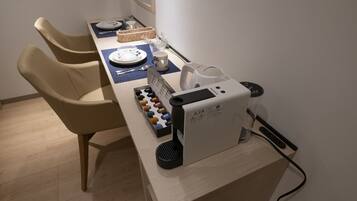 A dining area with a table set for two, a coffee machine, and a basket of bread.