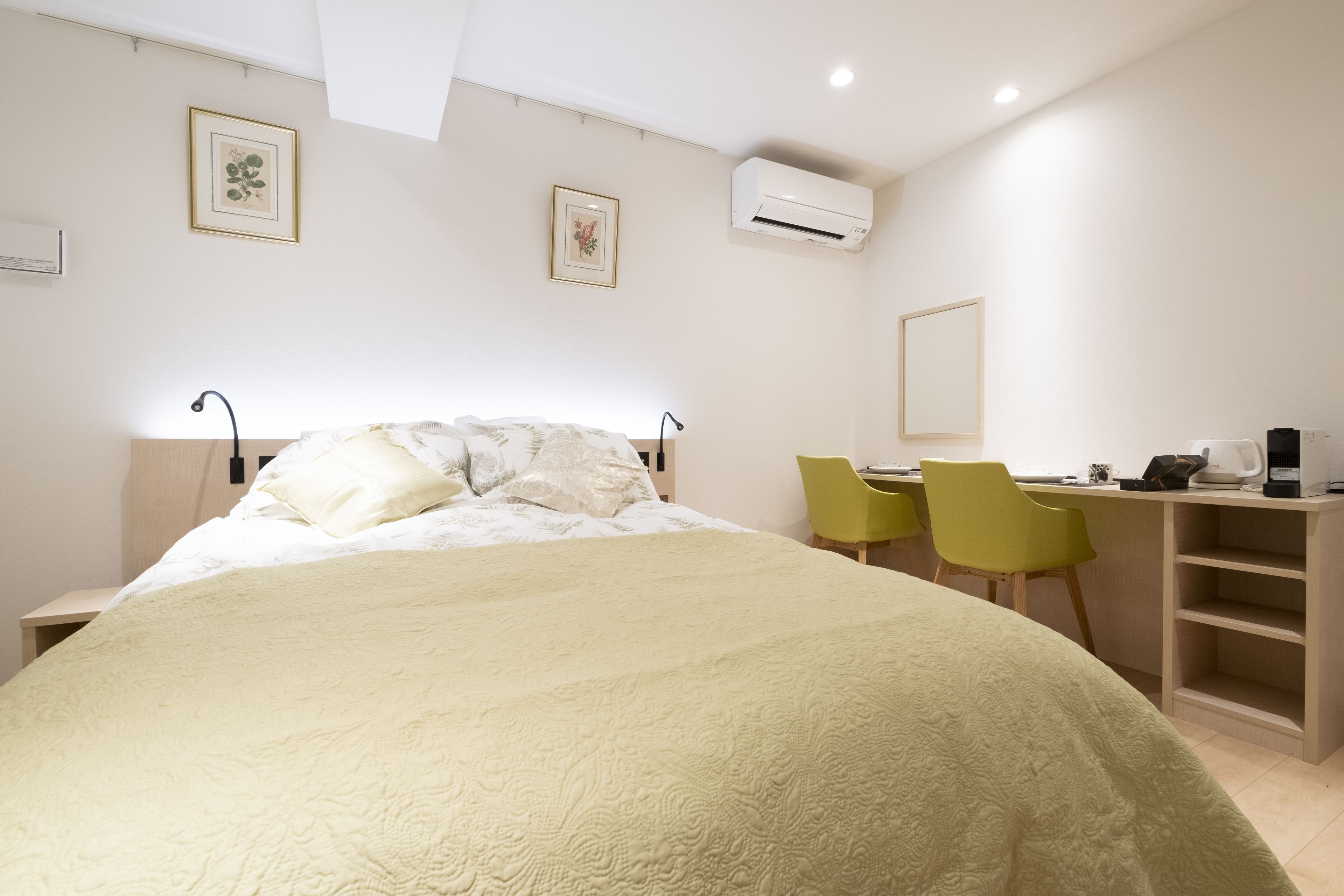 A bedroom with a bed, a desk, two chairs, and an air conditioning unit.