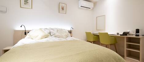 A bedroom with a bed, a desk, two chairs, and an air conditioning unit.