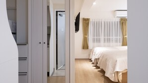A modern bedroom with a large mirror, a wardrobe, a bed with a white bedspread, and a window with sheer curtains. - STUDIO INN NISHISHINJUKU (Tokyo)
