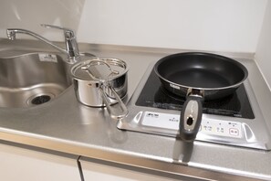 A kitchen with a stainless steel sink, a pot with a lid, and a frying pan on an induction cooktop. - STUDIO INN NISHISHINJUKU (Tokyo)