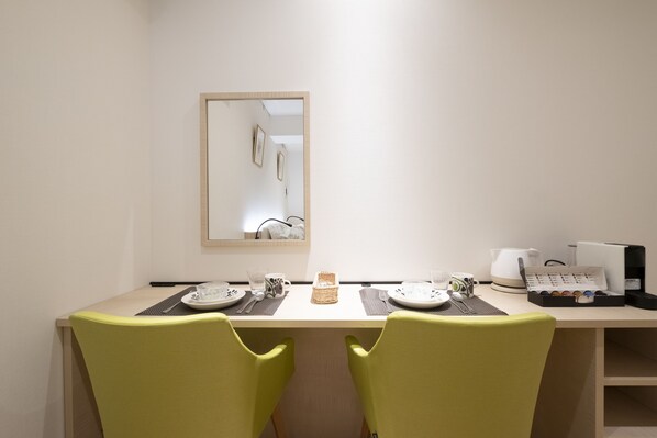 A dining area with two chairs, a table set with plates, cutlery, and a basket. A coffee machine and a kettle are on the table.