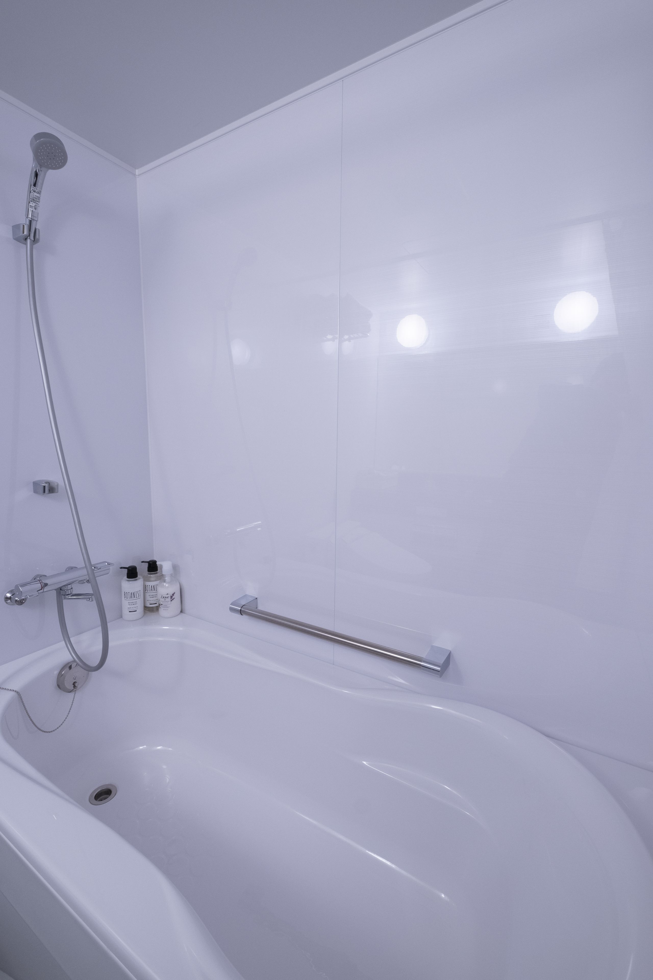 Un baño moderno con una bañera blanca, un cabezal de ducha manual y una mampara de cristal.