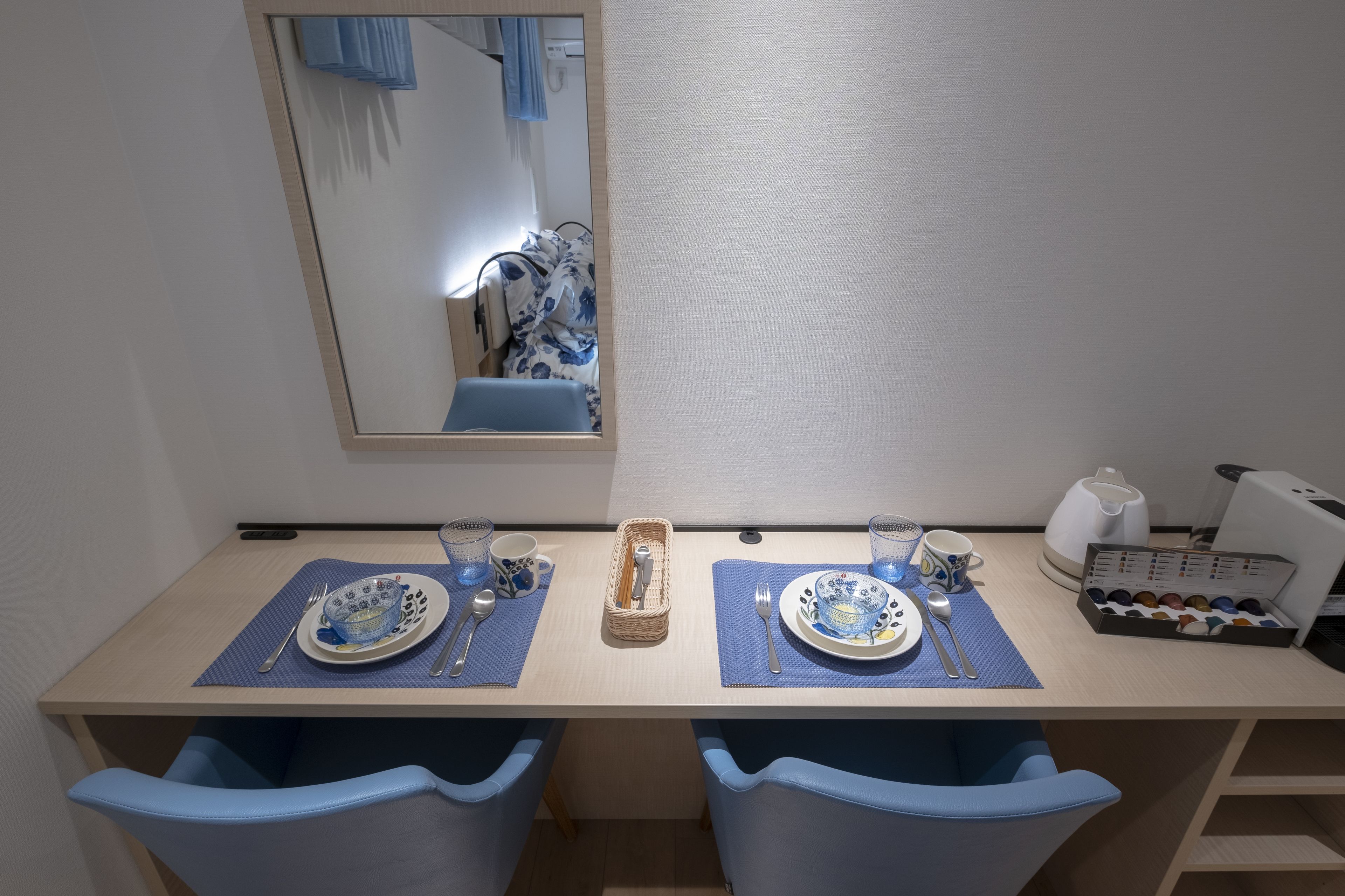 A dining area with two blue chairs, a wooden table, and a mirror reflecting part of the room.