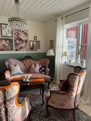 A cozy room with a tufted sofa, floral-patterned chairs, a wooden coffee table, and a chandelier. - Snöå Bruk Herrgård Hotell & konferens (Dala-Jarna)
