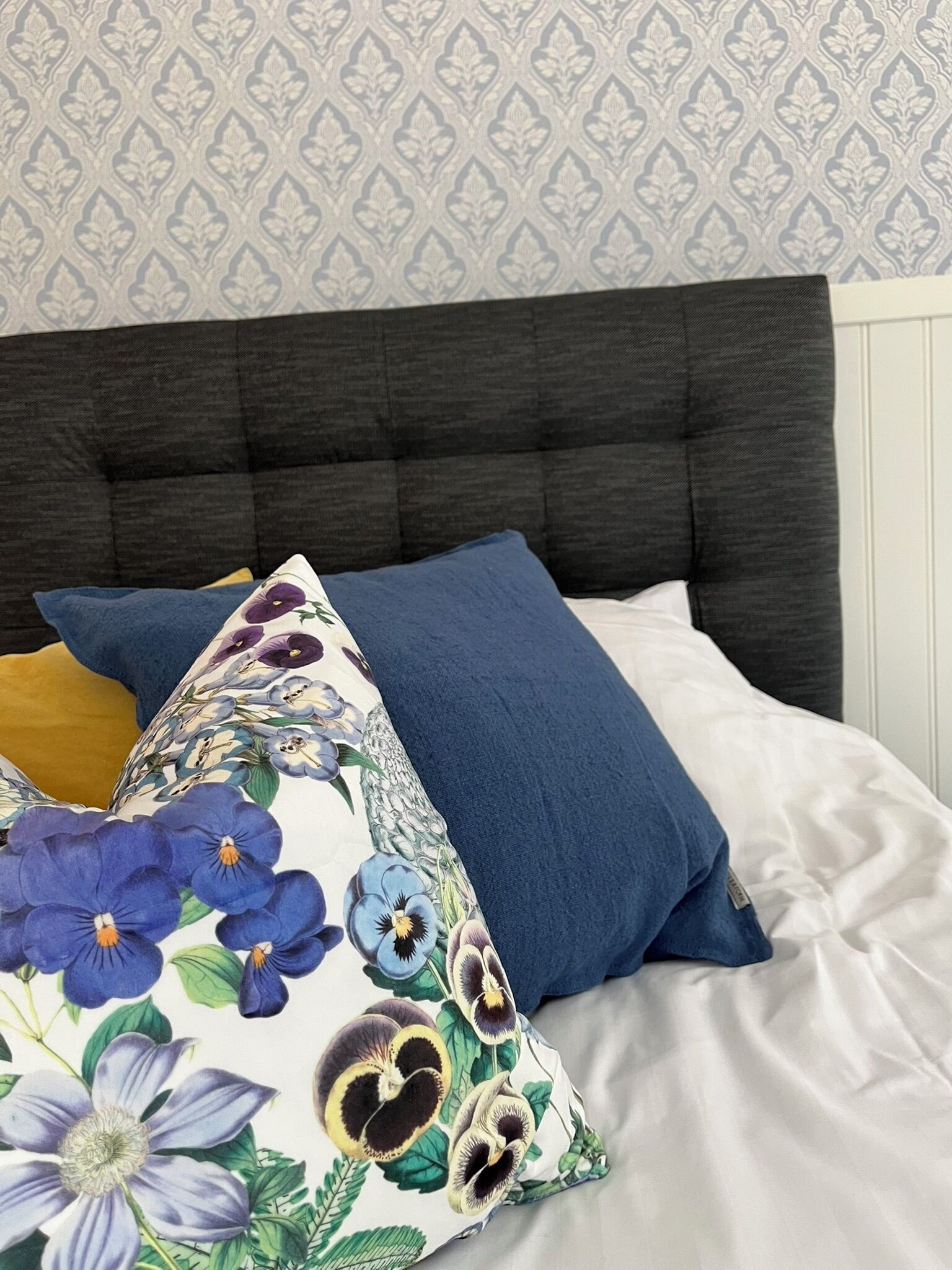 A bed with a dark headboard, white bedding, and decorative pillows with floral patterns.