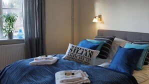 A neatly made bed with blue and white bedding, a pillow with text, a lamp, and a window with a plant. - Snöå Bruk Herrgård Hotell & konferens (Dala-Jarna)