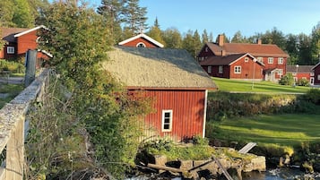 A red barn with a thatched roof, surrounded by greenery and a small stream.